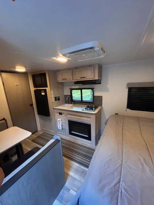 Inside this modern RV rental: a compact kitchen, dining area, and comfortable bed for your travels.. Heartland RVs Pioneer 2025