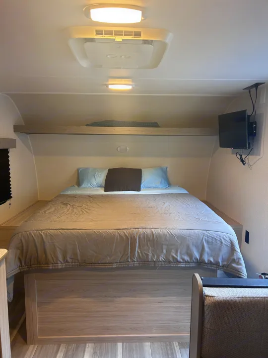 Cozy RV rental bedroom with a comfortable bed, overhead shelf, and wall-mounted TV, perfect for a relaxing getaway.. Heartland RVs Pioneer 2025
