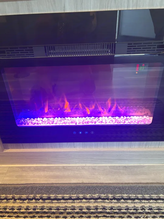 Cozy electric fireplace in an RV rental, showing purple flames, crystal media, and a temperature of 83°F.. Heartland RVs Pioneer 2025