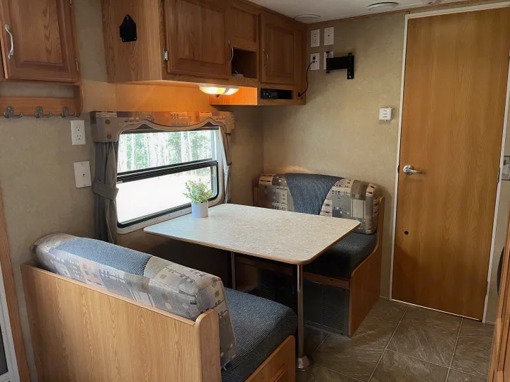 Inside a spacious RV rental: a cozy dinette with patterned benches, wooden cabinets, a window with tree views, and a wooden door.. Crossroads RV Sunset Trail 2008