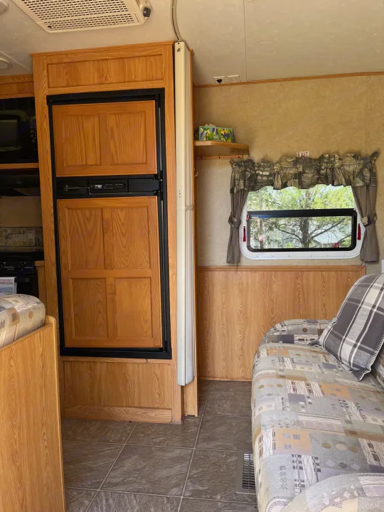 Cozy RV rental interior: kitchen appliances, wood paneling, sofa with patterned cushions, and a scenic window view.. Crossroads RV Sunset Trail 2008