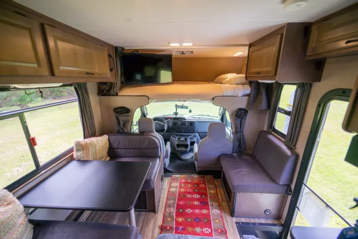Spacious rv rental interior with a cozy dinette, driver's cockpit, and an overhead bunk bed with a TV. Ready for adventures!. Thor Majestic 2018