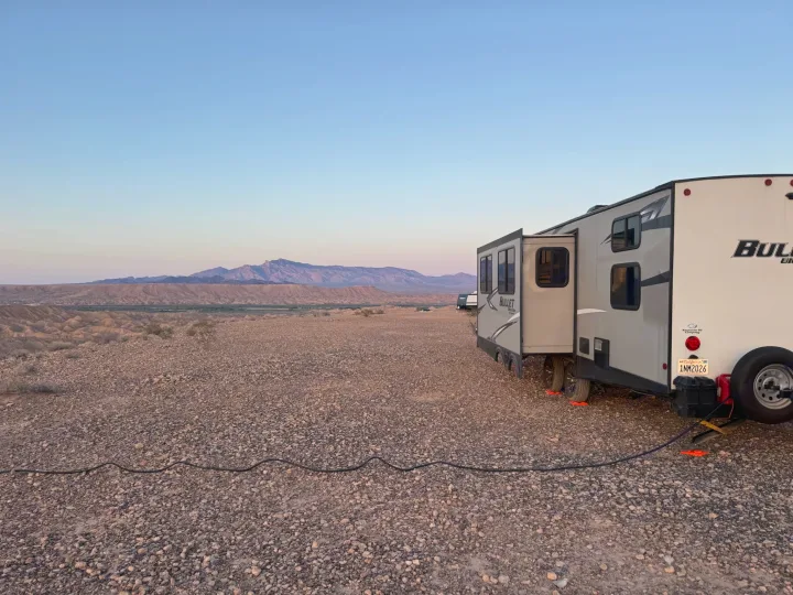 Experience freedom with an RV rental! A travel trailer is boondocking in a vast rocky desert, with mountains under a clear sky.. Keystone RV Bullet Ultra Lite 2021