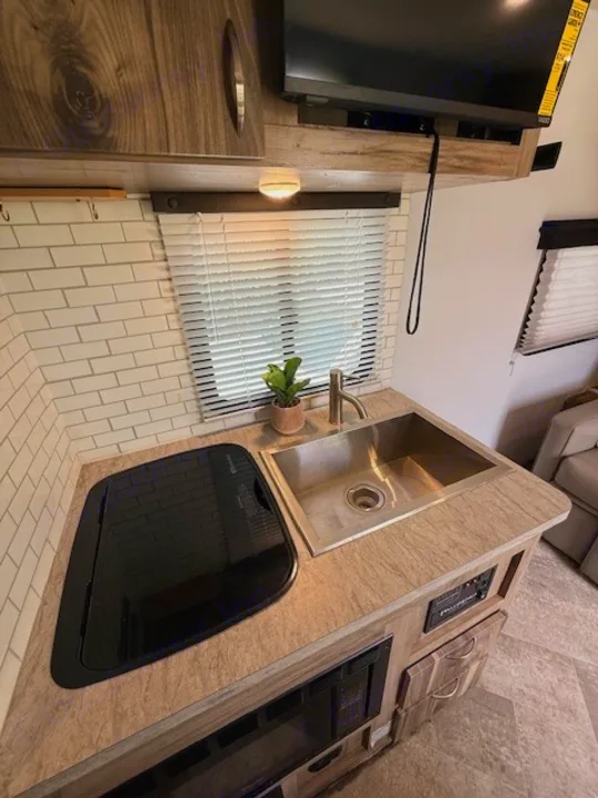 Bright rv rental kitchen with a sleek sink, covered stove, and microwave, plus a TV, ready for your adventures.. Forest River Palomino Real-Lite Mini 2021