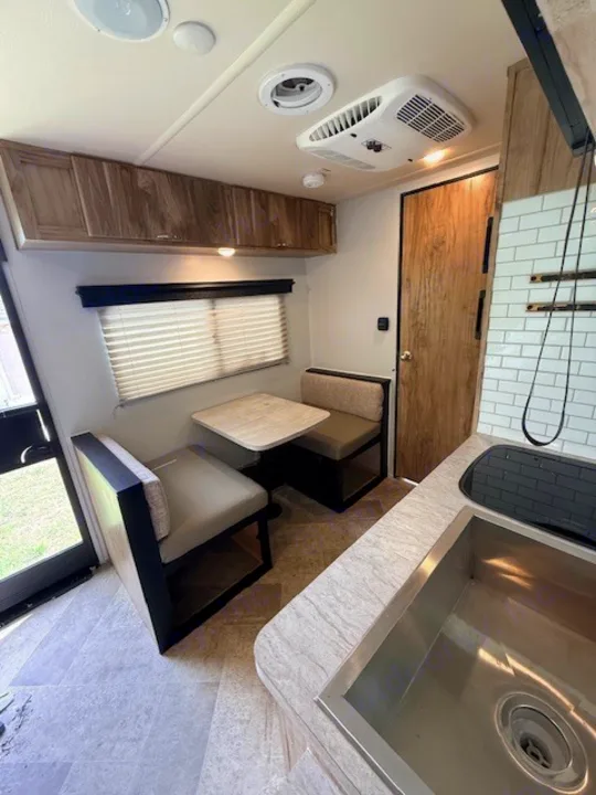 Clean RV rental interior with a light-colored dinette and table, stainless sink, and wooden cabinets. Ready for your adventure.. Forest River Palomino Real-Lite Mini 2021