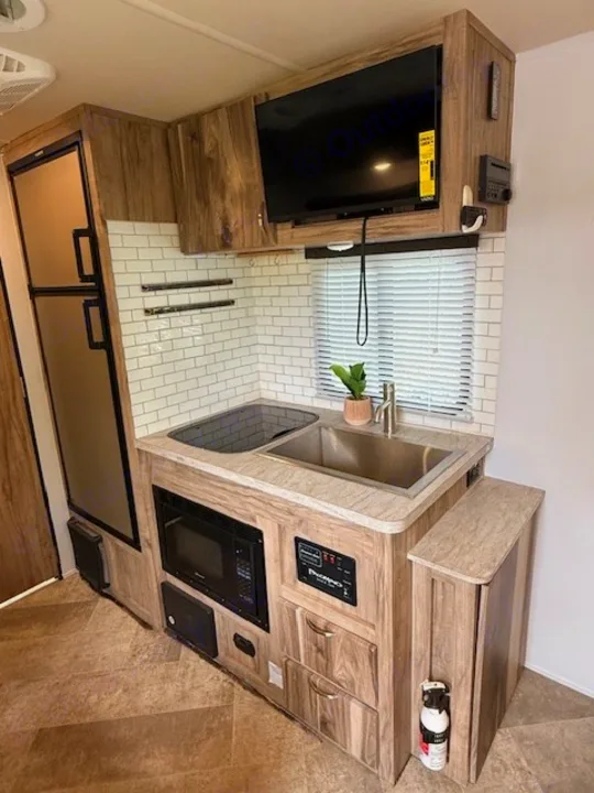 Well-appointed RV rental interior with a compact kitchen: fridge, microwave, sink, TV, and subway tile backsplash.. Forest River Palomino Real-Lite Mini 2021