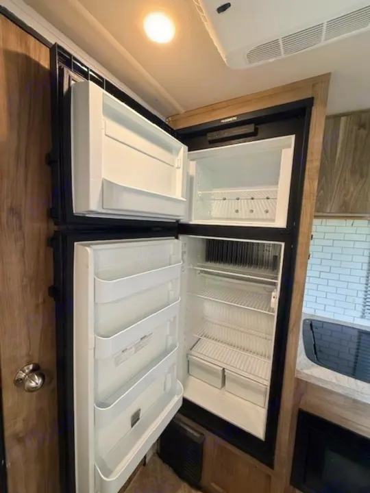Inside an rv rental: a clean, open Dometic refrigerator and freezer, with shelves and door bins, ready for your groceries.. Forest River Palomino Real-Lite Mini 2021