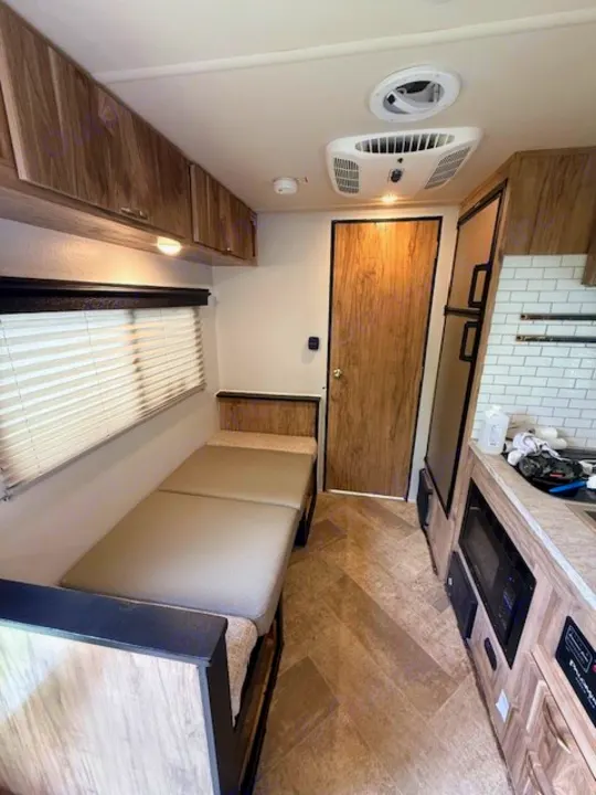 Inside this RV rental: compact living space with convertible bench/bed, kitchenette, overhead cabinets, and ceiling AC.. Forest River Palomino Real-Lite Mini 2021