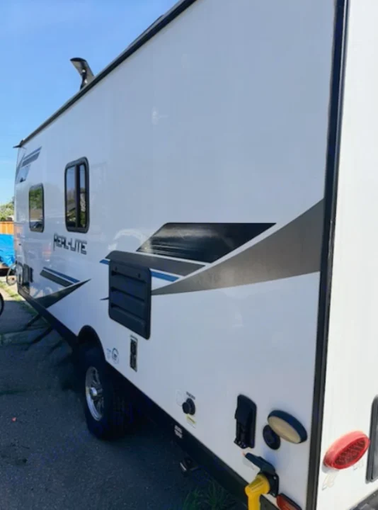 Modern PERL-LITE travel trailer, white exterior with bold graphics & visible utility hookups. Ideal for your next rv rental.. Forest River Palomino Real-Lite Mini 2021