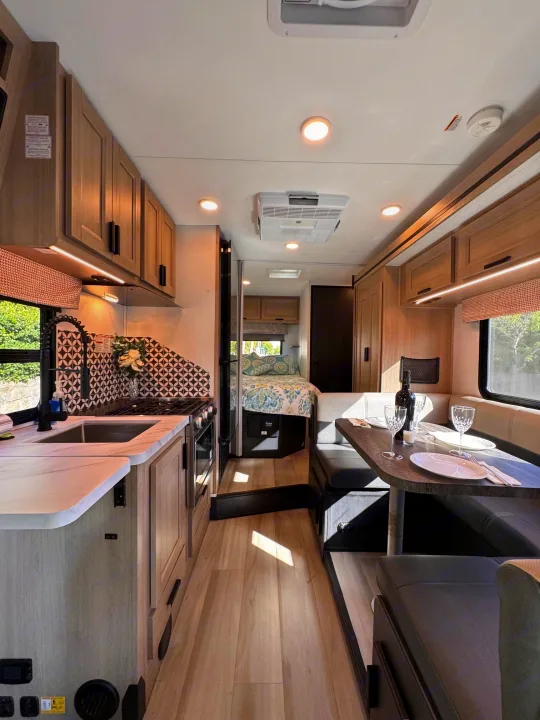 Spacious rv rental interior: kitchen with patterned backsplash, dining booth with wine, and comfortable bedroom.. Forest River Sunseeker LE 2025