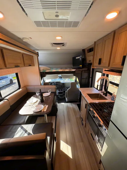 Explore this bright rv rental interior: full kitchen, dining booth, and comfy over-cab bed, ready for adventures.. Forest River Sunseeker LE 2025