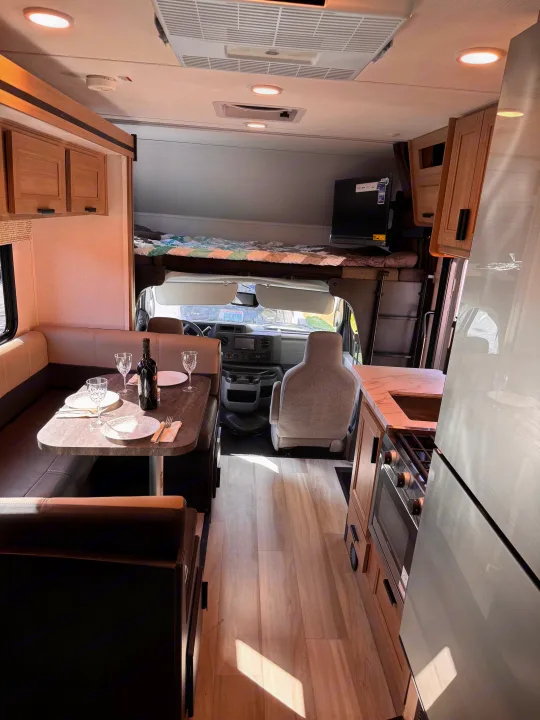 Bright RV rental interior showing a dining booth with wine, a full kitchen, and overhead bed. Ready for adventure.. Forest River Sunseeker LE 2025