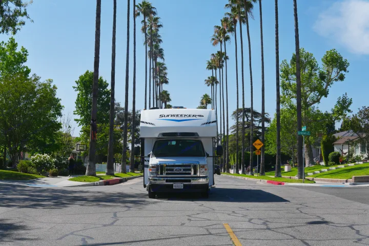 A white rv rental is parked in the middle of a sunny palm-lined street, with residential houses visible in the background.. Forest River Sunseeker LE 2025