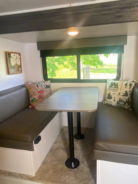 Inside an RV rental: a grey dinette with two benches, a table, and a window view of trees. Camping pillows add charm.. Keystone RV Hideout 2022
