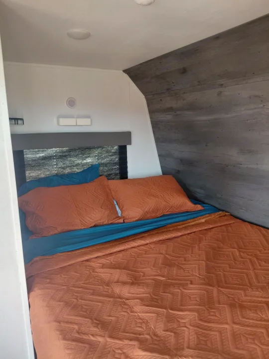 Cozy RV rental bedroom with orange quilted bedding, blue sheets, and modern decor, perfect for travel accommodations.. Keystone RV Hideout 2022
