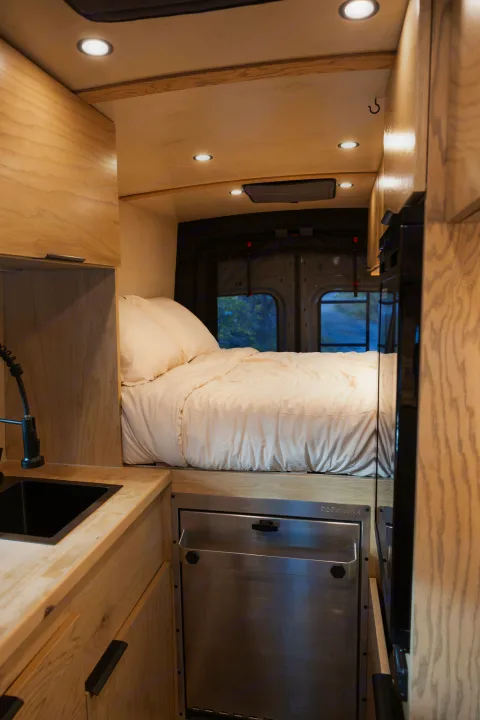Modern RV rental camper van interior featuring a sleek kitchen, cozy bed, and custom wooden cabinetry. Perfect for vanlife adventures.. Ford Transit 2022