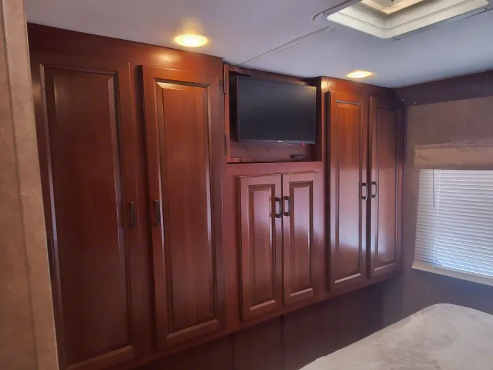 RV rental bedroom featuring dark wood cabinets, a mounted TV, and window with blinds, offering ample storage.. Forest River forester 2016
