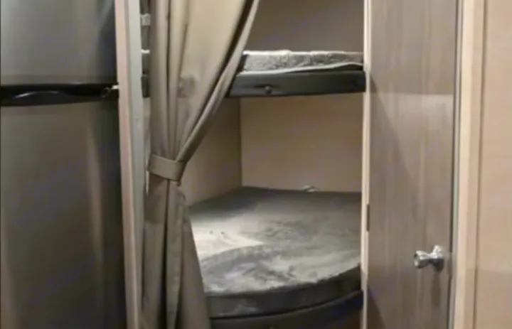 RV rental: compact interior with two bunk beds with gray mattresses, a silver refrigerator, and a tied-back privacy curtain.. Coachmen Catalina Summit 2022