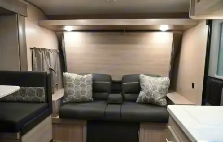 RV rental interior: Compact living space with a gray sofa, patterned pillows, a dinette on the left, and overhead lighting.. Coachmen Catalina Summit 2022
