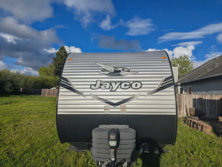 Bright front view of a Jayco RV rental travel trailer, gray and black with silver stripes, parked on grass under a cloudy sky.. Jayco Jay Flight SLX 2025