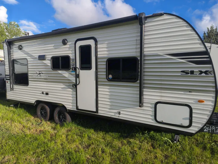 Exterior view of a modern grey and white Jay Flight SLX travel trailer for RV rental, parked on vibrant green grass.. Jayco Jay Flight SLX 2025