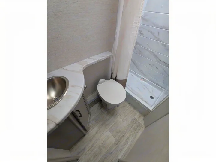 Compact RV rental bathroom: features a stainless steel sink, toilet, and shower with marble-look panels and light wood-grain floor.. Thor Chateau 2025