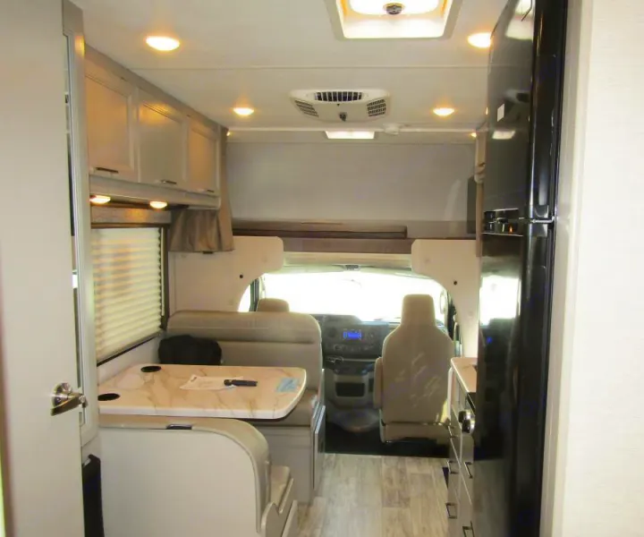 Inside this RV rental: a cozy dinette, fridge, and overhead storage. The driver's cab and a bunk above are visible for road trips.. Thor Chateau 2025