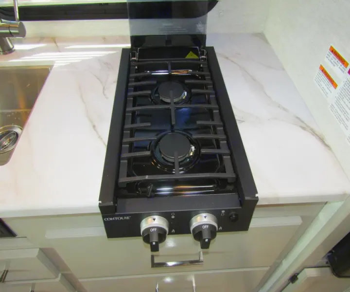 This RV rental kitchen features a modern two-burner gas stove, sink, and marble-look countertop for easy cooking on the go.. Thor Chateau 2025