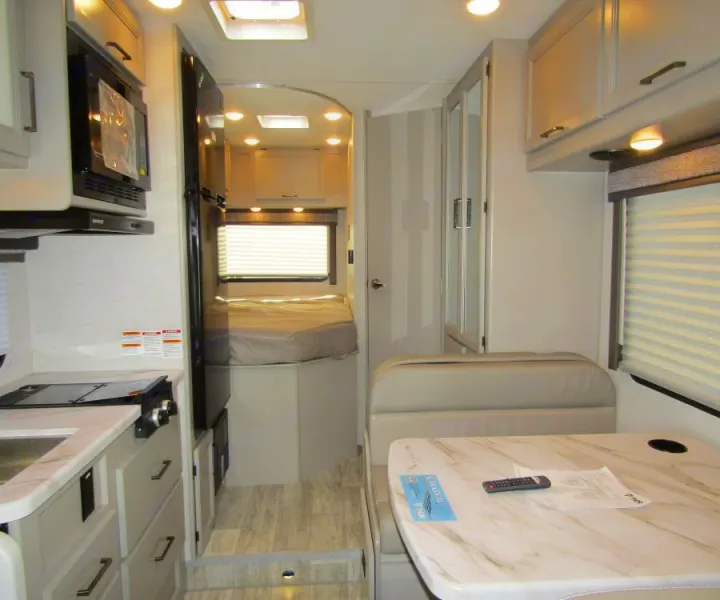 This RV rental interior features a cozy kitchen, a dinette with a marble-patterned table, and a rear bedroom setup.. Thor Chateau 2025
