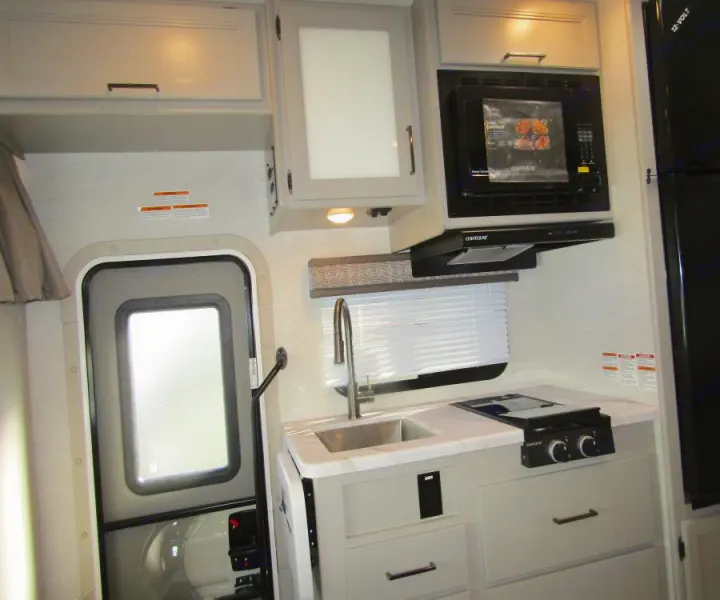 RV rental interior featuring a bright, compact kitchen with sink, stovetop, microwave, and entrance. Perfect for travel.. Thor Chateau 2025