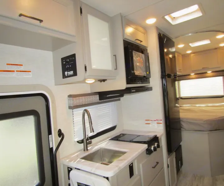Compact rv rental interior featuring a bright kitchen with a sink, stove, microwave, fridge, and a view of the bed area.. Thor Chateau 2025