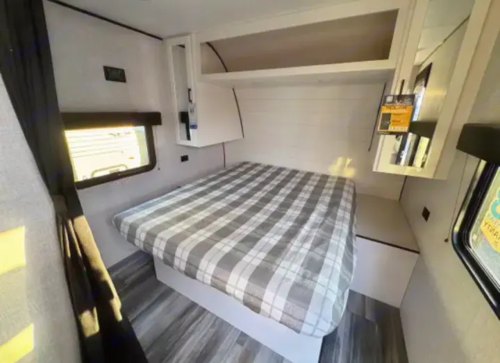 RV rental bedroom featuring a cozy plaid bed, white overhead cabinets, and bright windows. Ideal for travel comfort.. Jayco Jay Flight SLX 2025