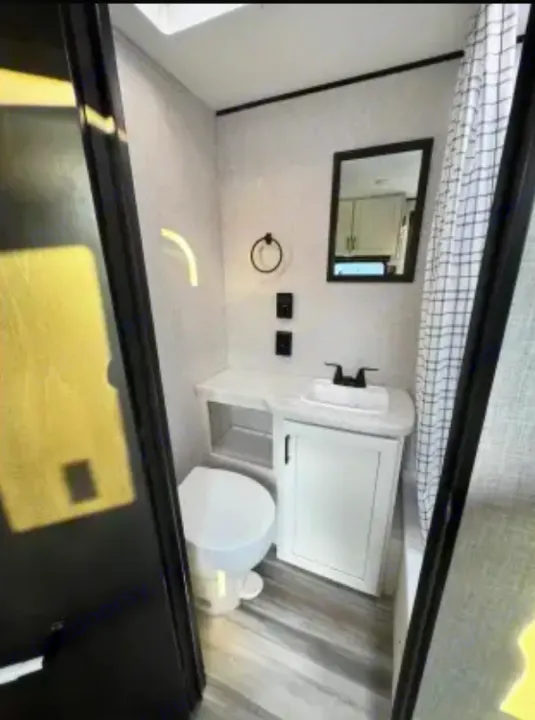 Inside a modern RV rental bathroom: toilet, sink vanity, mirror, and checker-patterned shower curtain for compact travel.. Jayco Jay Flight SLX 2025