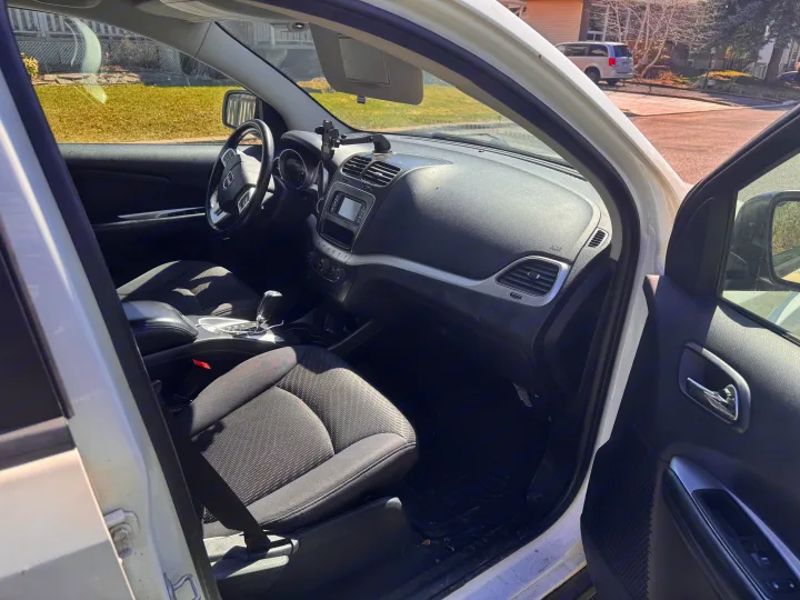 View of a clean white car's driver side interior, featuring the dashboard, steering wheel, and fabric seats. Perfect for planning your rv rental trip.. Dodge Journey 2012
