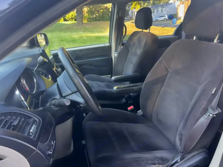 Interior view of an RV rental's front cabin showing black fabric seats, steering wheel, dashboard, and an outdoor scene.. Dodge Caravan 2014