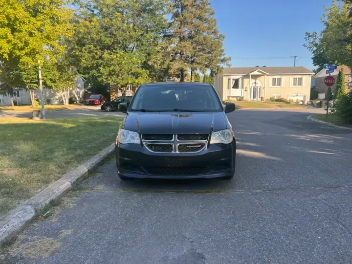 Considering an rv rental? This black minivan is parked on a sunny suburban street, with houses and trees visible in the background.. Dodge Caravan 2014