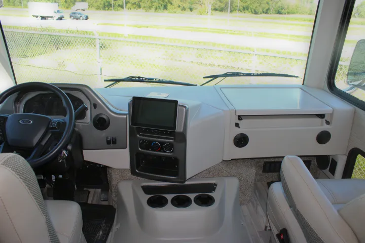 Inside an RV rental: driver's cockpit with Ford steering wheel, central display, climate controls, and passenger seat. Ready for adventure.. Thor Motor Coach Ace 2024