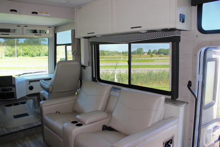 Spacious rv rental interior showing cream recliners, driver's seat, and overhead cabinets with scenic window views.. Thor Motor Coach Ace 2024