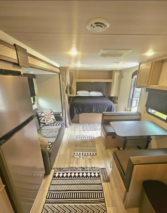 Modern rv rental interior featuring a bright bedroom, cozy dining area, and living space with stylish black & white rugs.. Keystone RV Springdale 2024