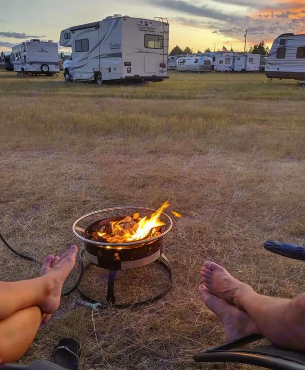 Barefoot relaxation by a warm campfire at sunset, with an RV rental and other campers in the background.. Dutchmen Coleman Lantern 2020