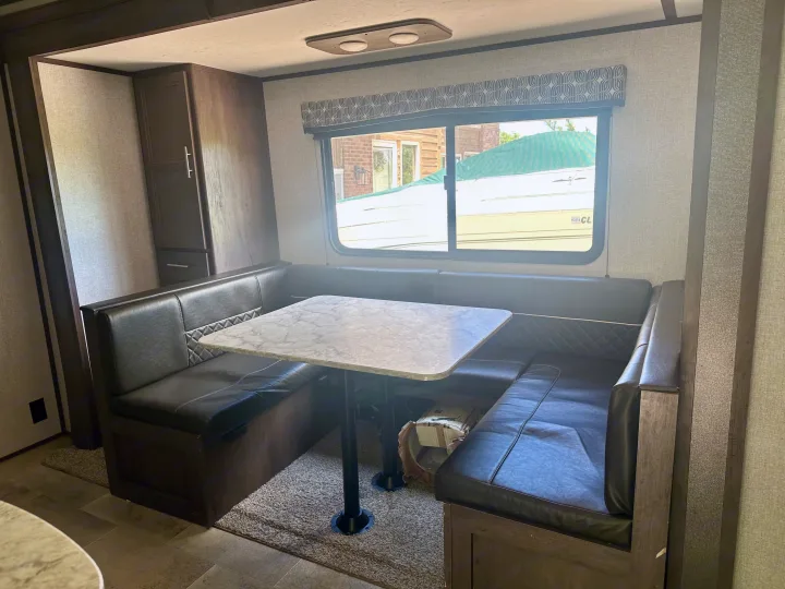 Explore this RV rental's dinette area, featuring comfortable U-shaped seating, a marble-pattern table, and large window.. Dutchmen Coleman Lantern 2020
