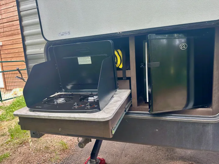 This RV rental's outdoor kitchen showcases a pull-out gas stove and compact refrigerator, perfect for camping meals.. Dutchmen Coleman Lantern 2020