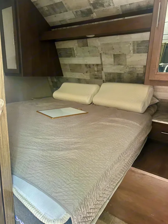 RV rental bedroom with a chevron-quilted bed, contour pillows, and rustic wood-paneled walls.. Dutchmen Coleman Lantern 2020