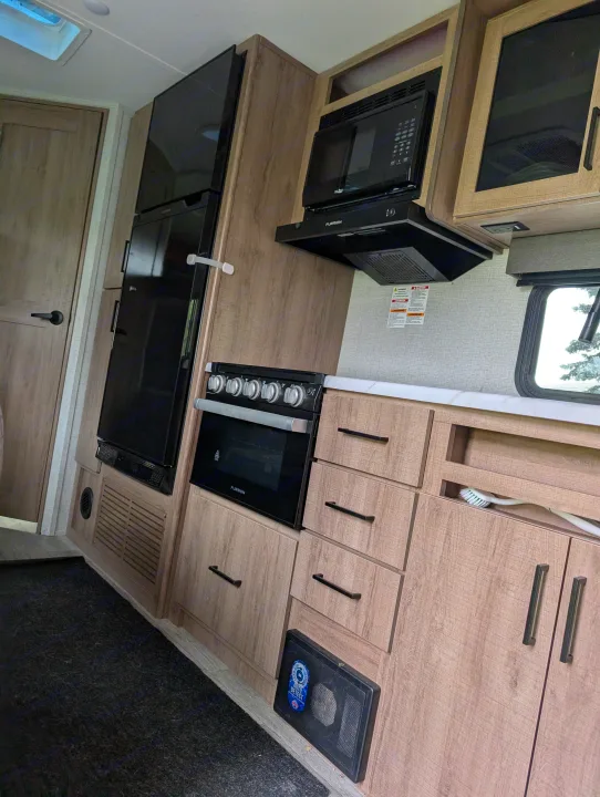 RV rental interior: Modern kitchen with a tall black fridge, microwave, oven, white counter, and light wood cabinetry.. Grand Design Imagine XLS 2023