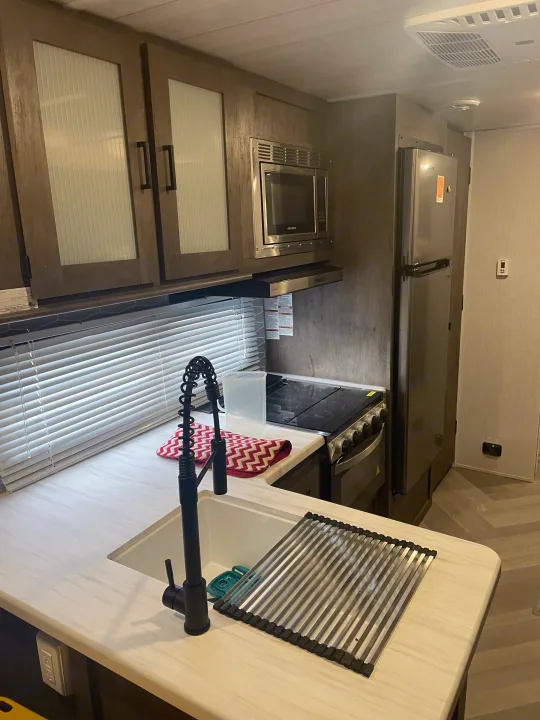Modern RV rental kitchen with sink, stove, microwave, and refrigerator. Includes overhead cabinets, blinds, and a spacious counter.. Forest River Salem 2022