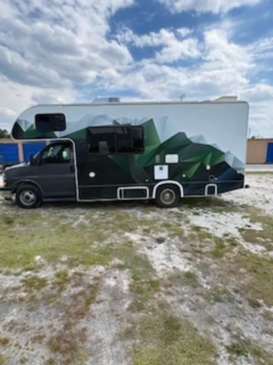 This custom-wrapped Class C RV rental, featuring a mountain design, is parked on a gravel lot, ready for adventure.. Thor Quantum LC 2022