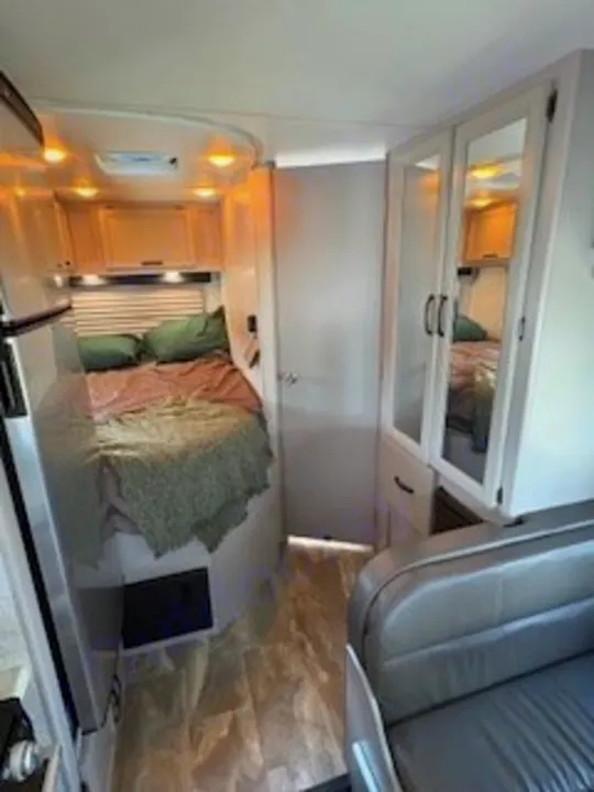 Modern RV rental interior showing a cozy bedroom, mirrored closet, and front living space for travel comfort.. Thor Quantum LC 2022