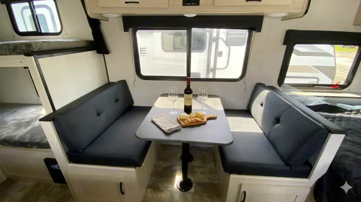 Cozy RV rental interior with a dinette, wine, cheese, and bunk beds, offering a comfortable space for camping adventures.. Coachmen Apex Nano 2023