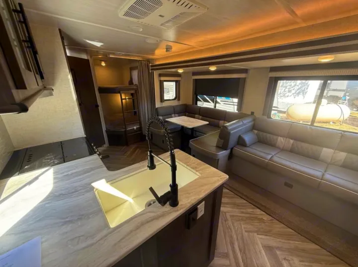 Spacious RV rental interior with a modern kitchen island, dining booth, comfy lounge sofa, and bunk beds for family adventures.. Forest River Salem 2022