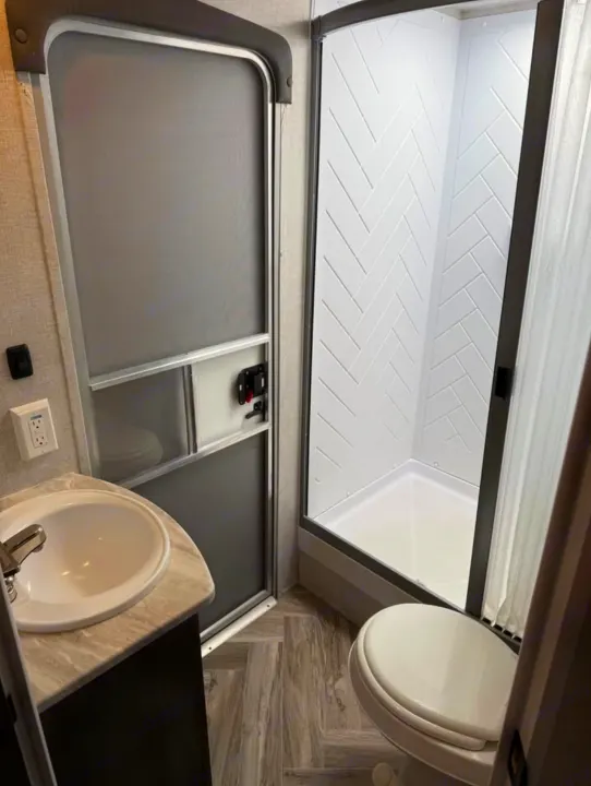 Compact RV rental bathroom: modern shower with herringbone walls, toilet, and sink vanity.. Forest River Salem 2022